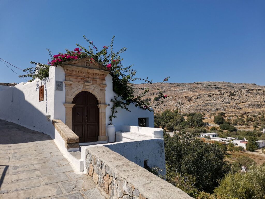 Pictureque white building with old door and sprawling purple flowered plant in Lindos, Rhodes, Greece