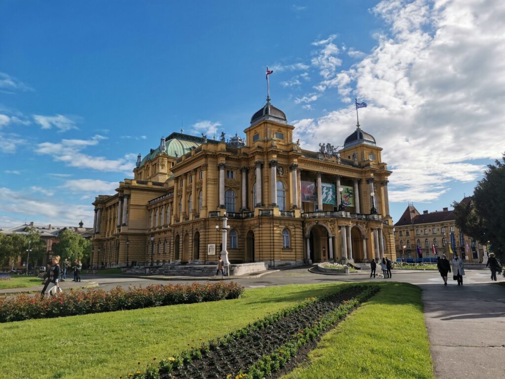 The Croatian National Theatre in Zagreb with blue skies above and green grass around it