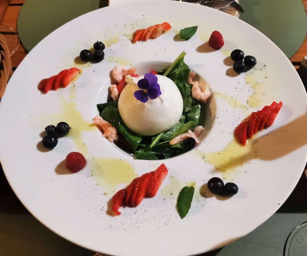 Beautifully composed dish of burata. Burata is in the centre on leaves with small prawns. Surrounded by slices of strawberry and blueberry. A beautiful dish served up in Dubrovnik restaurants
