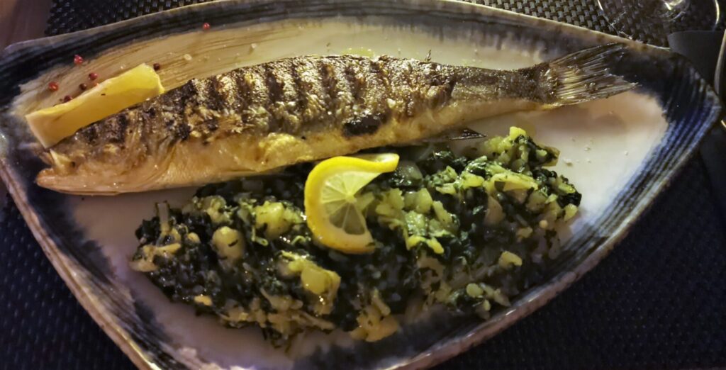 A grilled fish served on a nice blue and white plate with potato and chard.