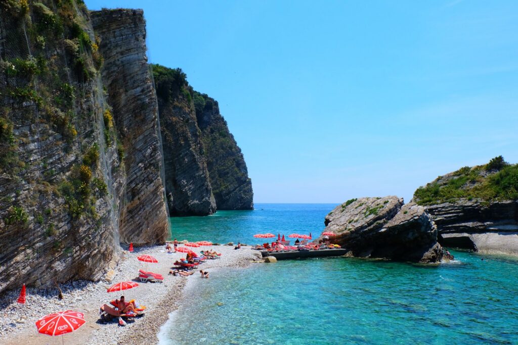 A sunny day on the beach with cliffs and red umbrellas at Sveti Nikola island in Montenegro