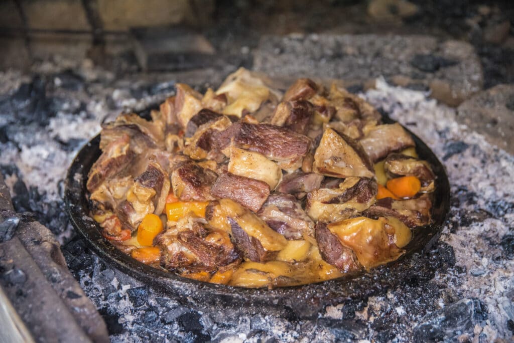 A hot iron pot resting on hot coals filled with Montenegro food of Ispod Saca