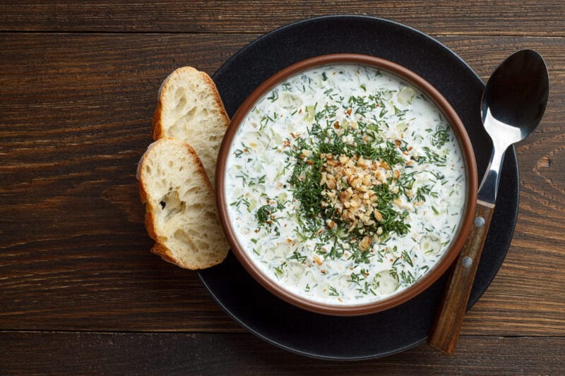 Chilled tarator with bread and spoon on wooden table ready to eat. Healthy summer refreshment soup with vegetables. Top view