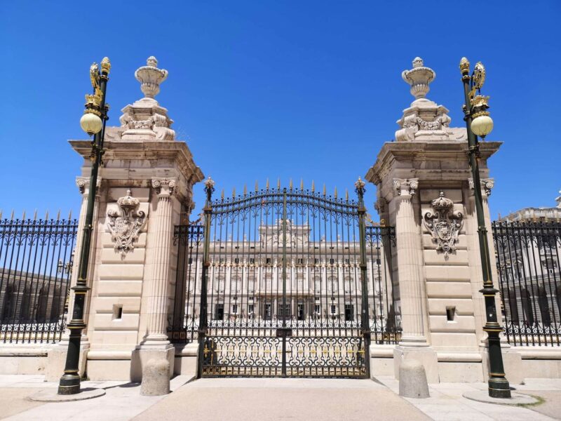 The grand Royal Palace gates in Madrid, Spain with iron work and stone details. Blue sky - top thing to do in Madrid itinerary