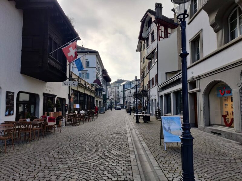 A view down one of the Old Town streets in Lucerne with old buildings lining either side of the cobbled streets and a Swiss flag on a building to one side