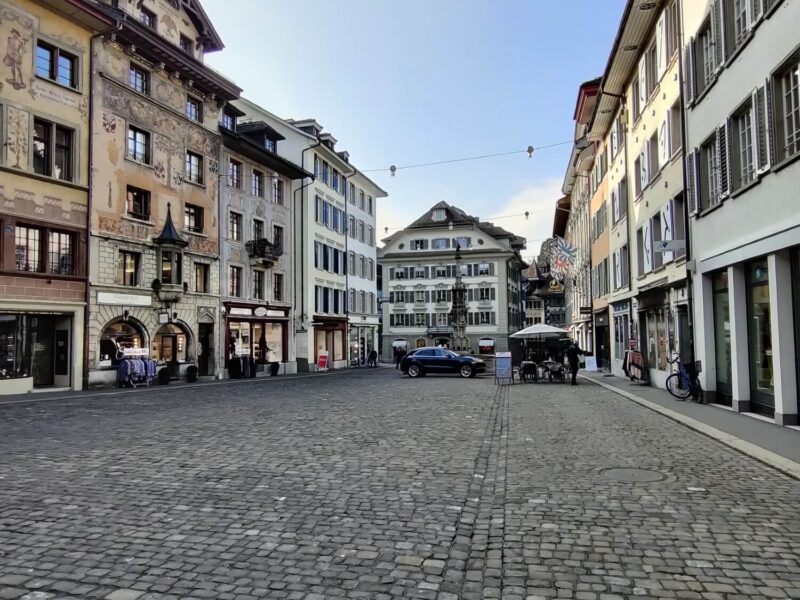 A large cobbled and quiet square in Lucerne Old Town with historical buildings all around in Swiss-German architectural style