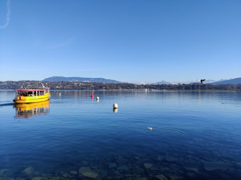 A still day on Lake Geneva with a yellow sightseeing boat at the forefront